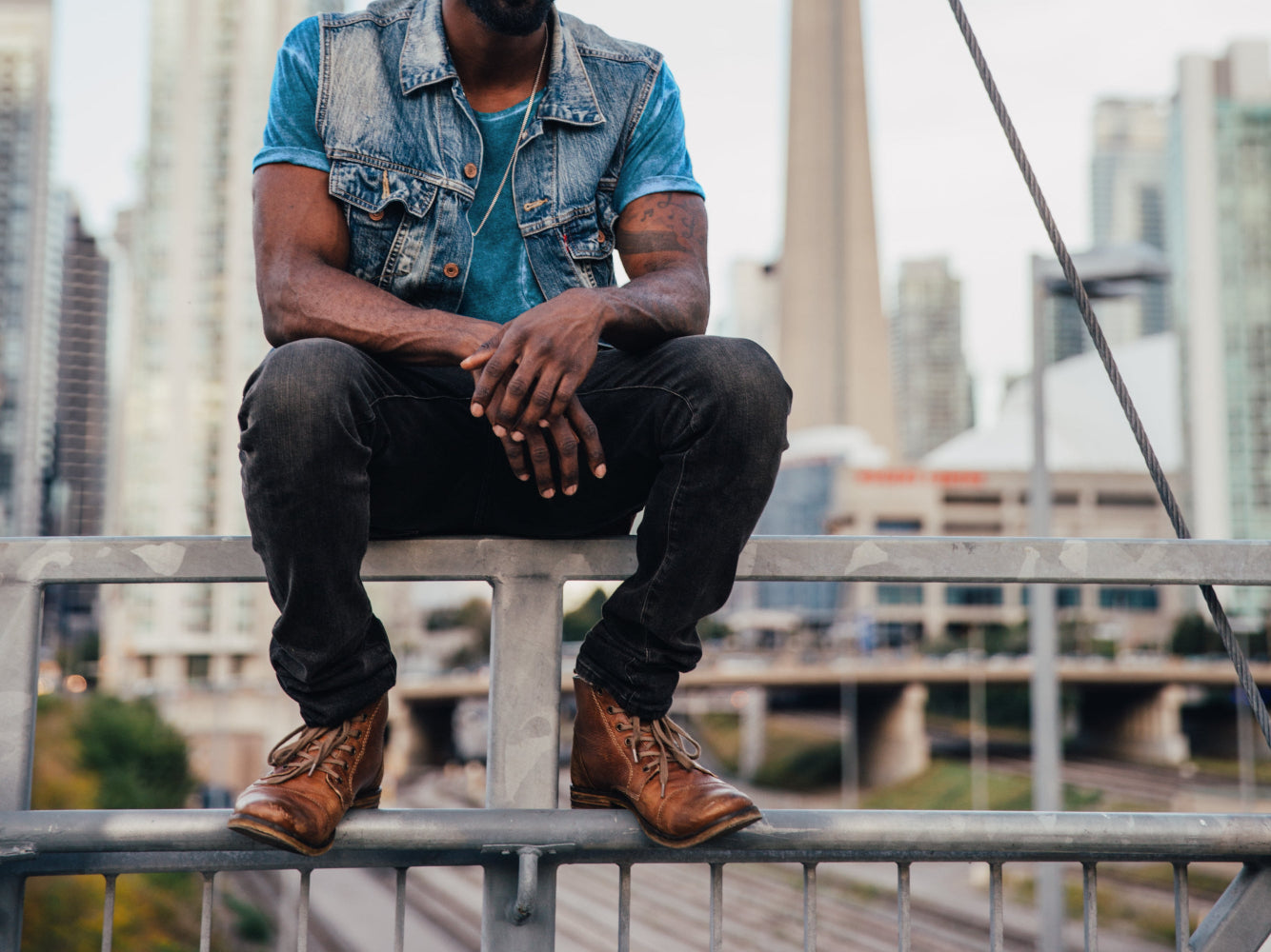 Man sitting on a railing with a cityscape background. The city never stops, pressure, noise, distractions everywhere but prayer changes everything.